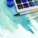 Paint brushes and a case of paints resting on a watercolor painting